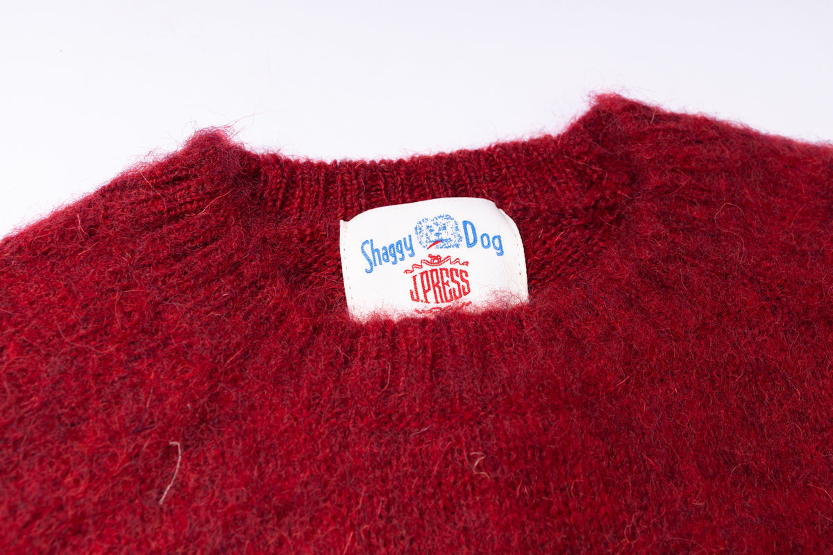 Close-up of a deep red fuzzy knit sweater with a white neck label reading 'Shaggy Dog J Press'.