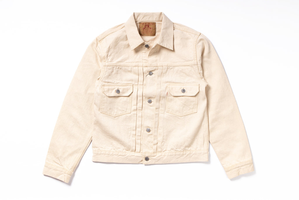A light beige denim trucker jacket with a button-up front, two buttoned chest flap pockets, and a classic collar, laid flat on a white background.