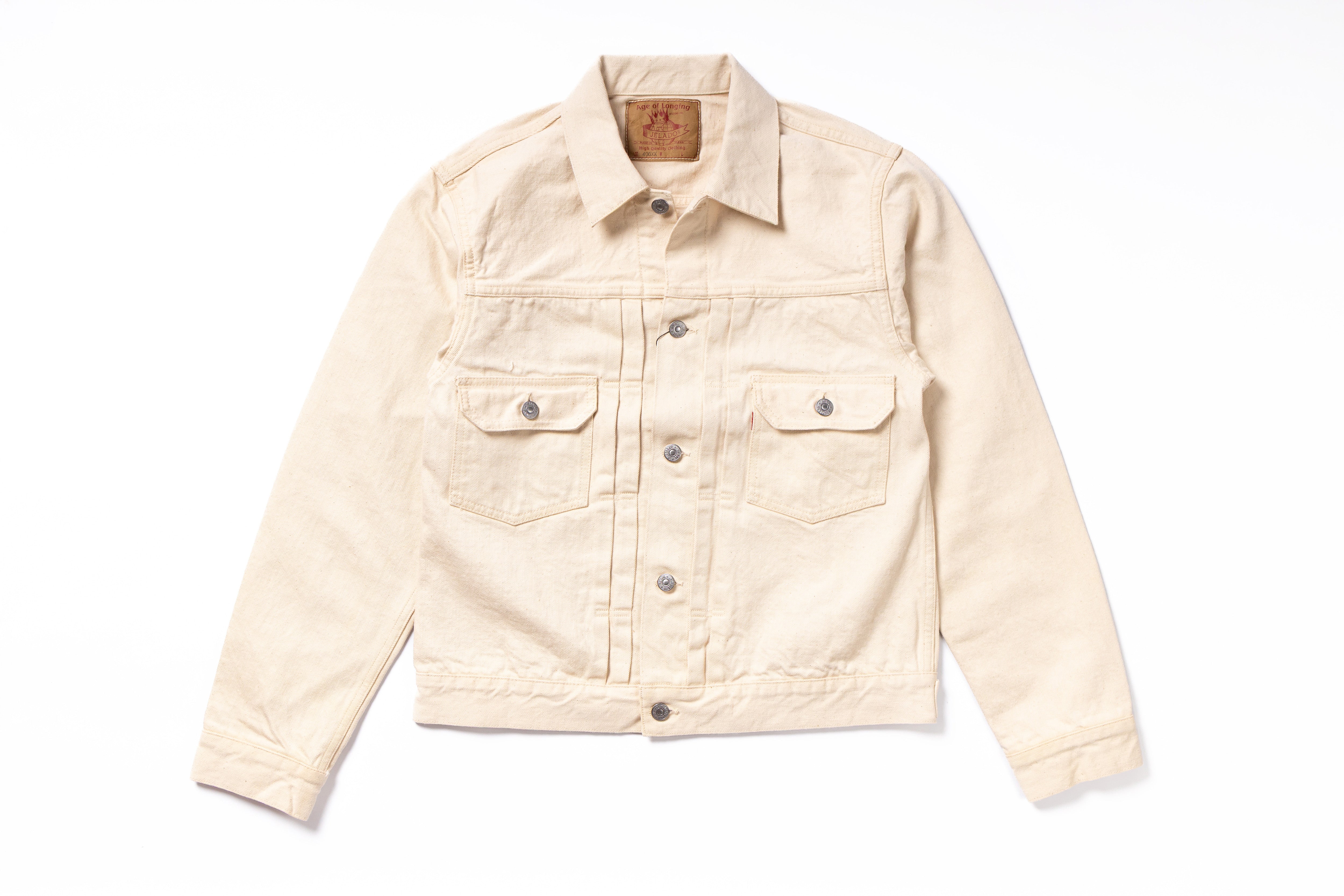 A light beige denim trucker jacket with a button-up front, two buttoned chest flap pockets, and a classic collar, laid flat on a white background.