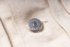 A close-up shot of a silver-toned metal snap button fastening a light beige or cream-colored canvas jacket.