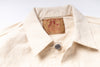 Close-up of a cream-colored cotton shirt collar with a visible vintage-style brand label reading 'Age of Learning' and 'JEANS' inside the collar, plus a single metal button at the neck.
