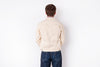 A man viewed from behind wearing a light beige canvas utility jacket and dark blue jeans, standing against a plain white background.