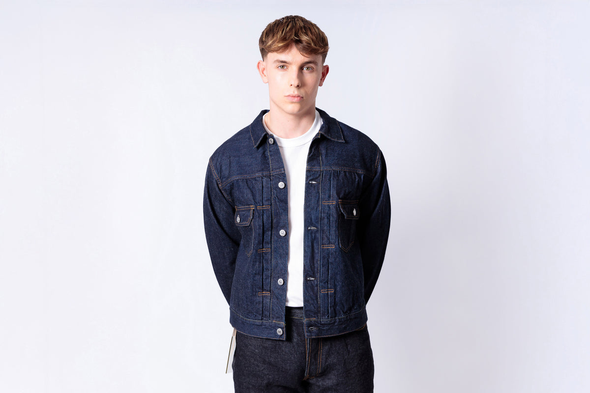 Man wearing a denim jacket over a white shirt on a light gray background
