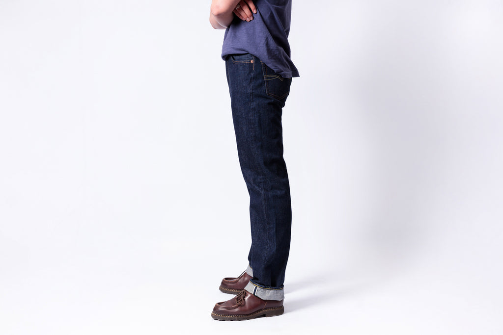 Person wearing dark blue jeans and brown shoes on a white background
