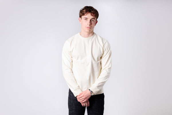 Person wearing a white sweater and dark pants against a plain background