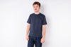 A man wearing a dark navy blue crewneck t-shirt and dark blue jeans, standing against a plain white studio background.