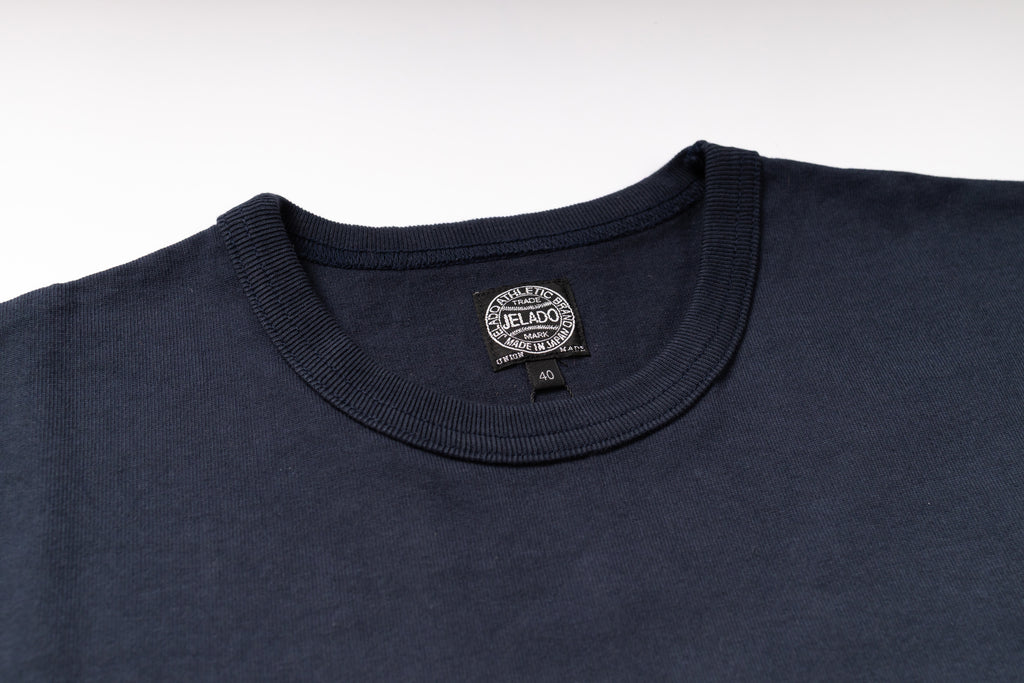 Close-up of a dark navy blue crewneck t-shirt showing the inner neck label which reads 'JELADO'.