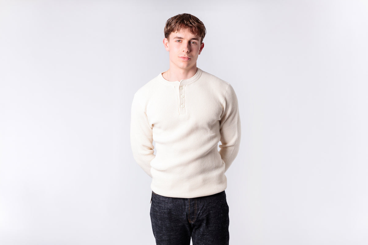 Man wearing a cream sweater and dark jeans against a white background