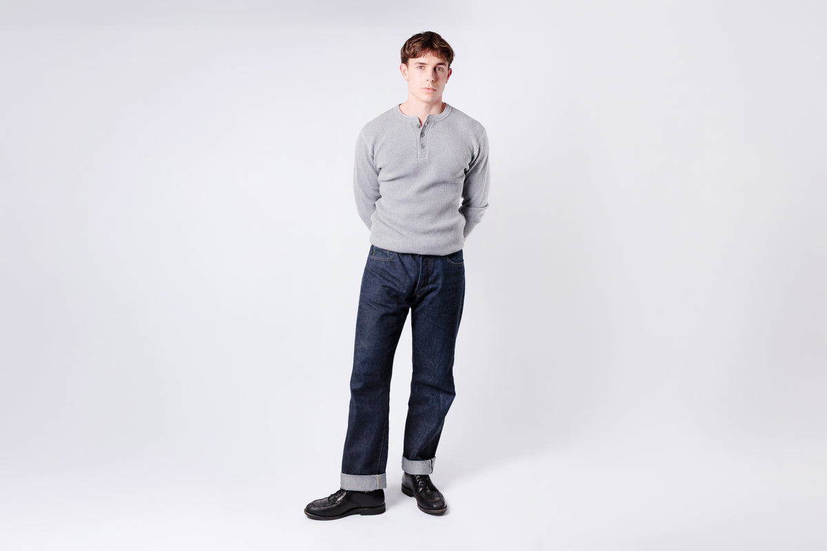 Man wearing a gray sweater and dark pants on a white background