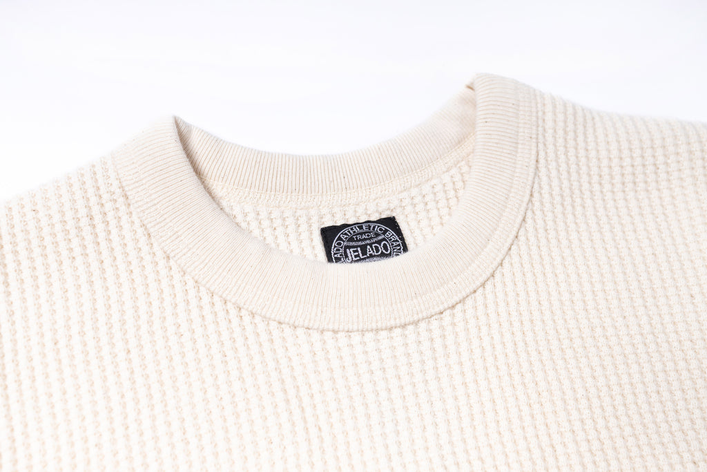 Close-up of a cream-colored sweater with a brand label on a white background