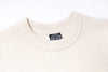 Close-up of a cream-colored sweater with a brand label on a white background