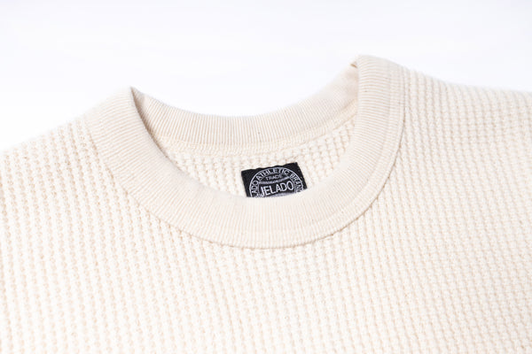 Close-up of a cream-colored sweater with a brand label on a white background