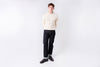 Man wearing a cream sweater and dark pants on a white background