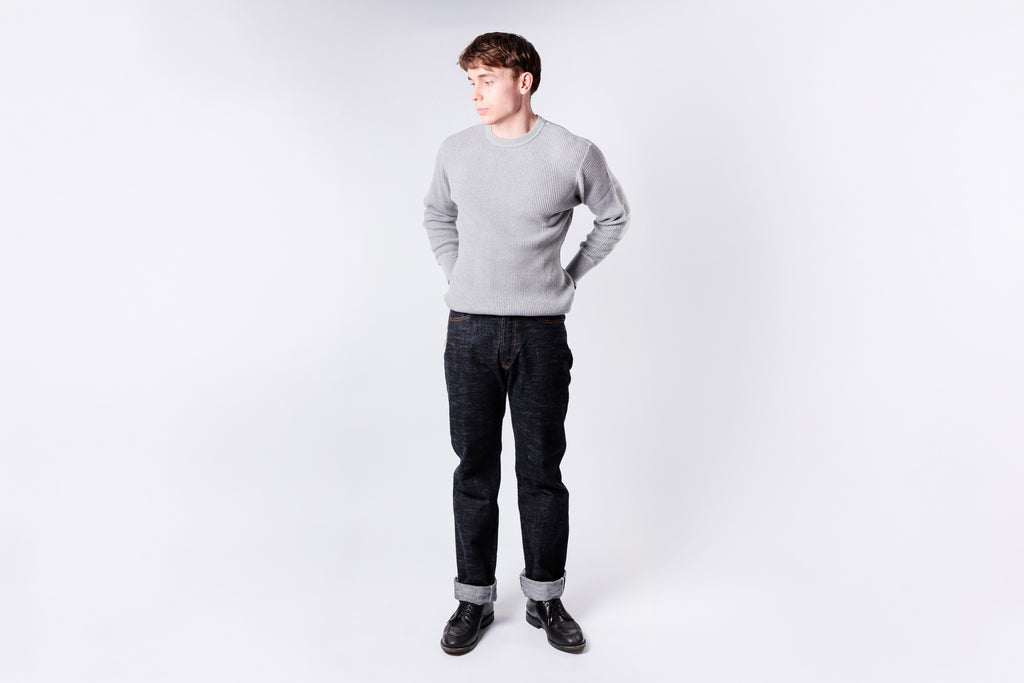 Man wearing a gray sweater and dark jeans on a white background