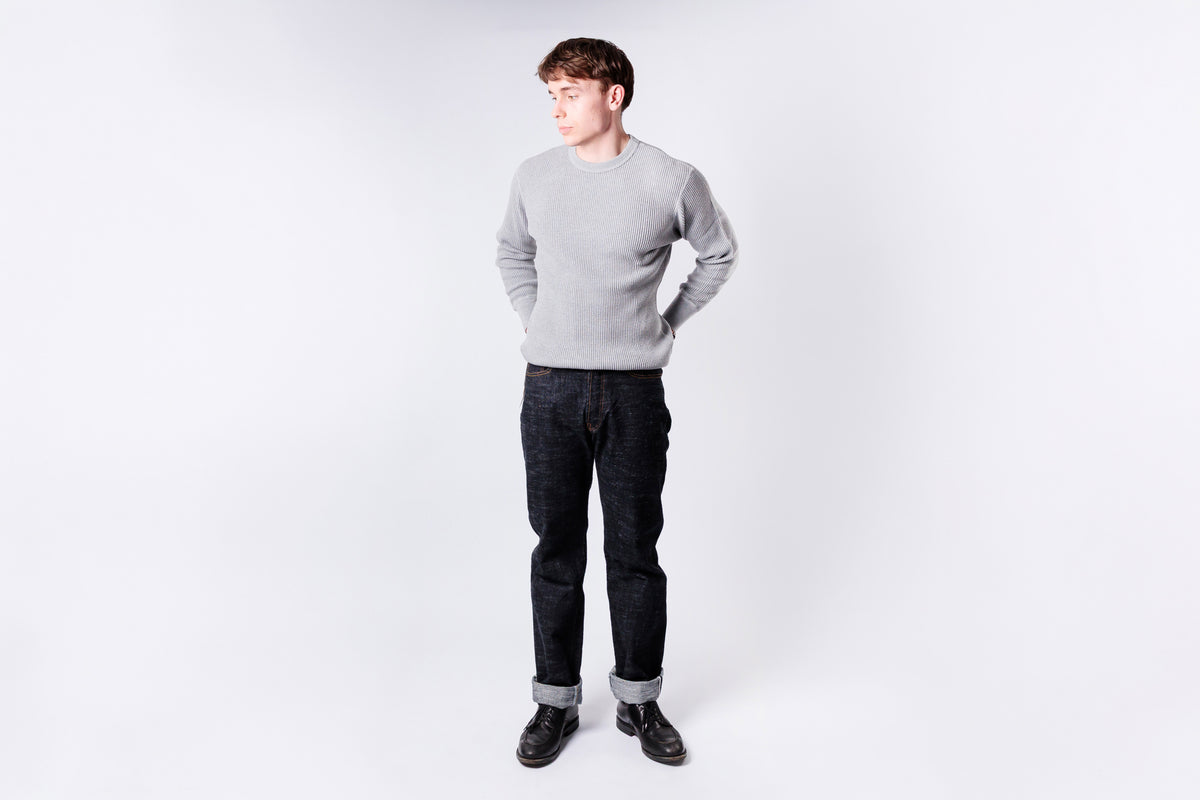 Man wearing a gray sweater and dark jeans on a white background