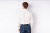 A man viewed from behind wearing a white long-sleeve button-up shirt and blue jeans against a plain white background.