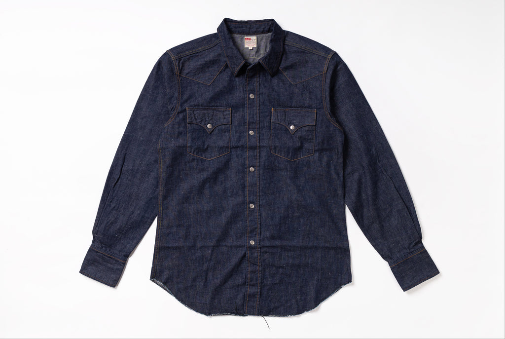 A dark indigo denim western-style shirt jacket with two buttoned chest pockets, laid flat on a white background.
