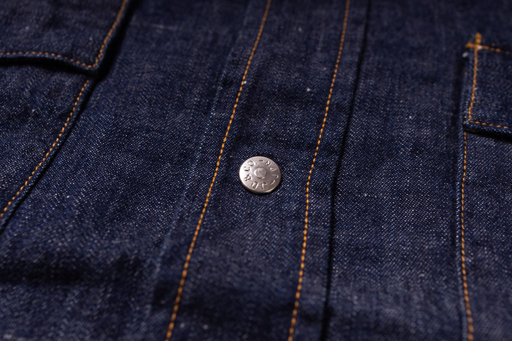 Close-up of dark indigo denim fabric with orange contrast stitching and a round silver metal button.