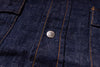 Close-up of dark indigo denim fabric with orange contrast stitching and a round silver metal button.