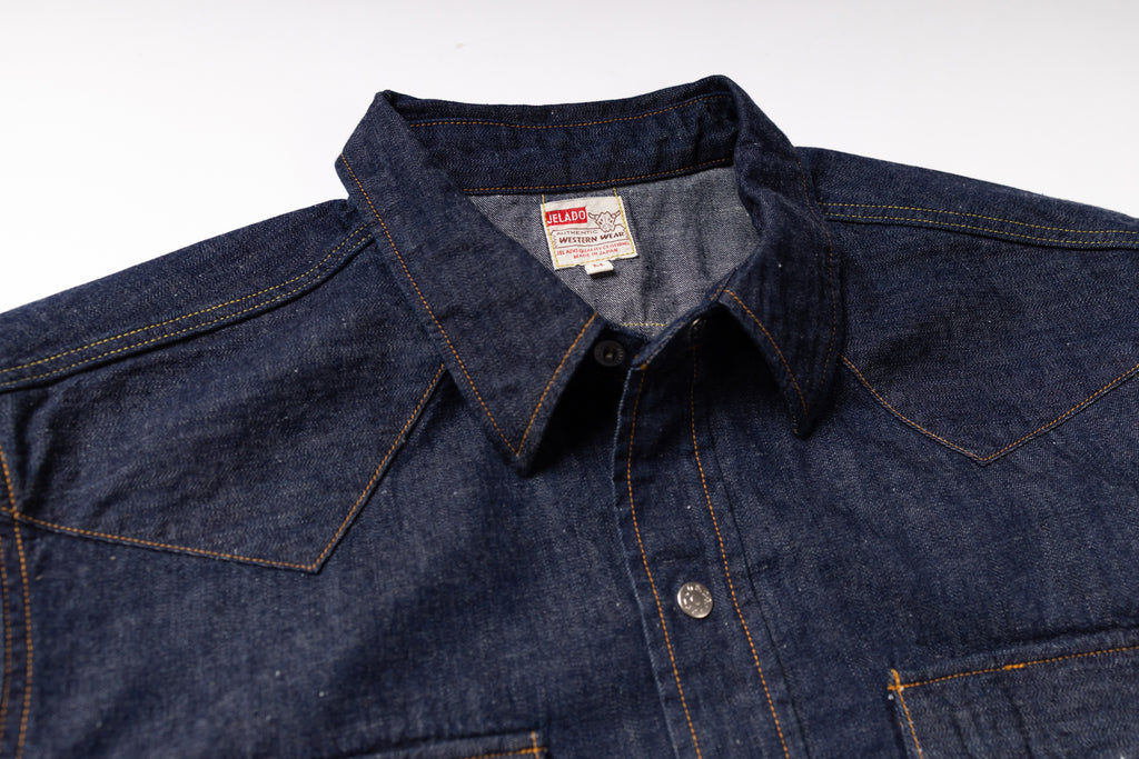 Close-up of a dark indigo denim shirt jacket with contrast orange stitching, a pointed collar, and a visible U.S.