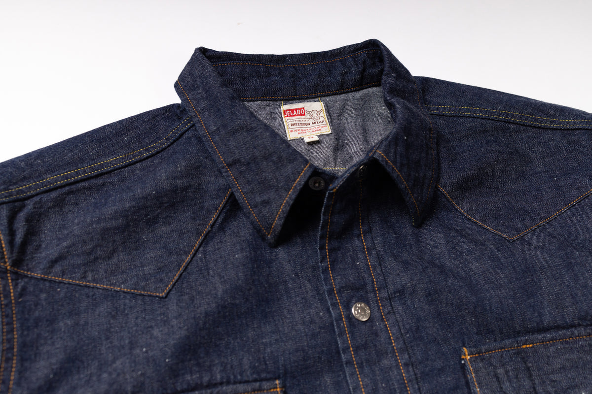 Close-up of a dark indigo denim shirt jacket with contrast orange stitching, a pointed collar, and a visible U.S.