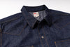 Close-up of a dark indigo denim shirt jacket with contrast orange stitching, a pointed collar, and a visible U.S.