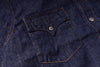 Close-up of a dark indigo denim garment showing a buttoned chest pocket with contrast orange stitching and a silver metal button.