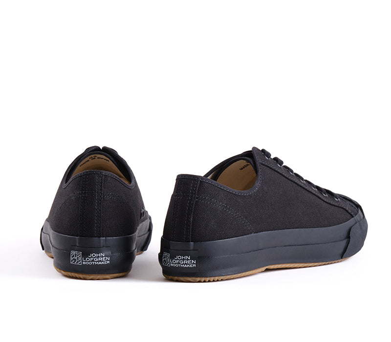 A pair of black low-top canvas sneakers shown from the rear three-quarter angles on a clean white background.