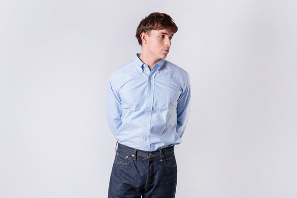 A man wearing a blue oxford shirt on a white background