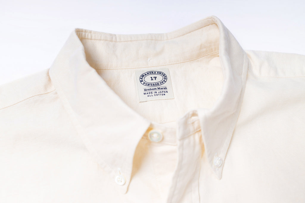 Close-up of a ecru shirt with a visible label on a light gray background