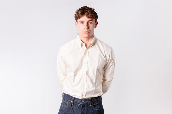 A man wearing a ecru oxford shirt on a white background