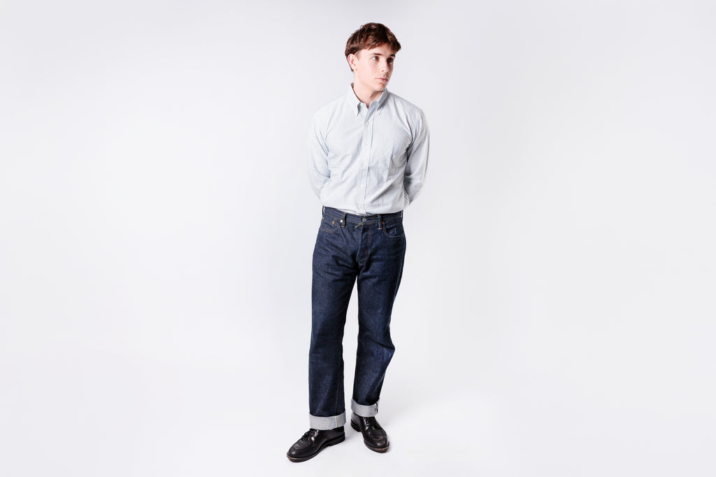 Person wearing a light blue shirt and dark jeans on a white background