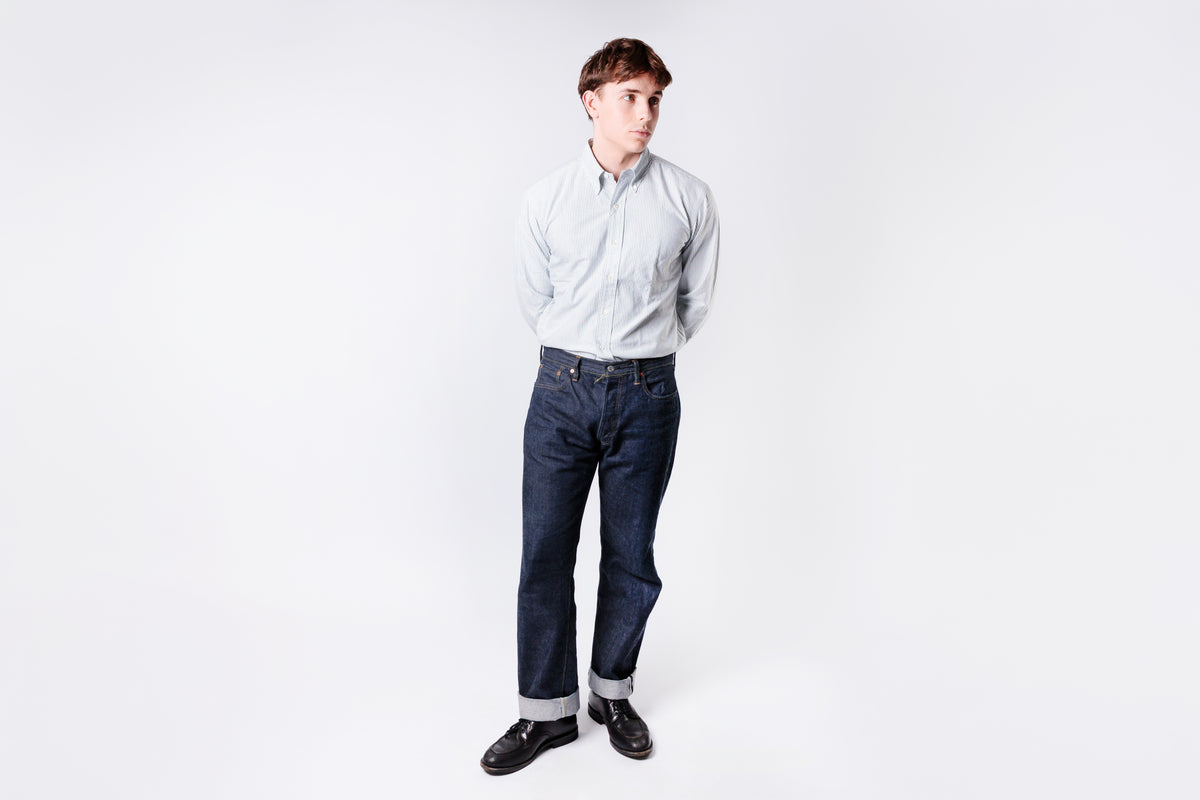 Person wearing a light blue shirt and dark jeans on a white background