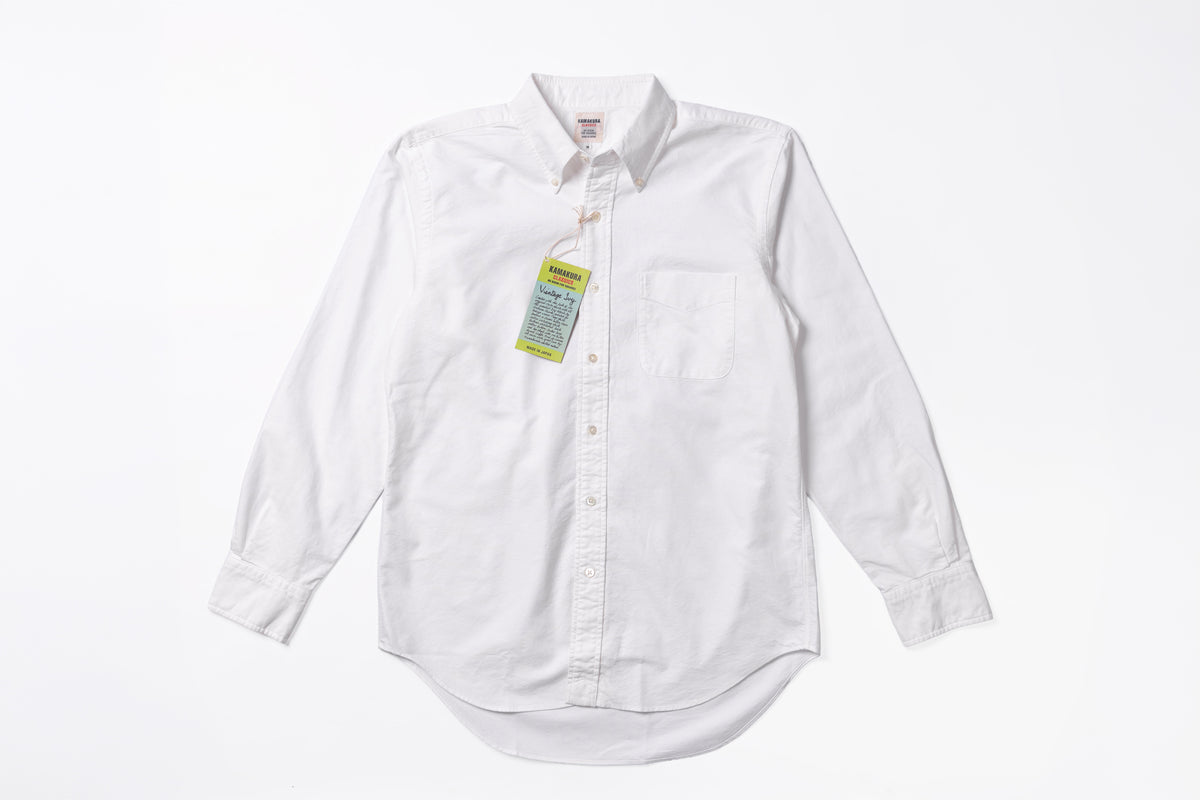 A white long-sleeve button-down shirt with a chest pocket, laid flat on a white background with a yellow and green hangtag attached.