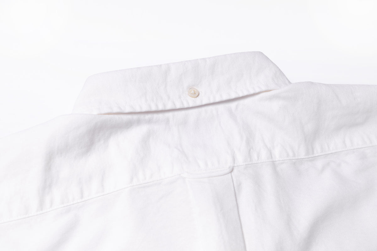 Close-up of a white button-down shirt collar with a single button, shown against a plain white background.