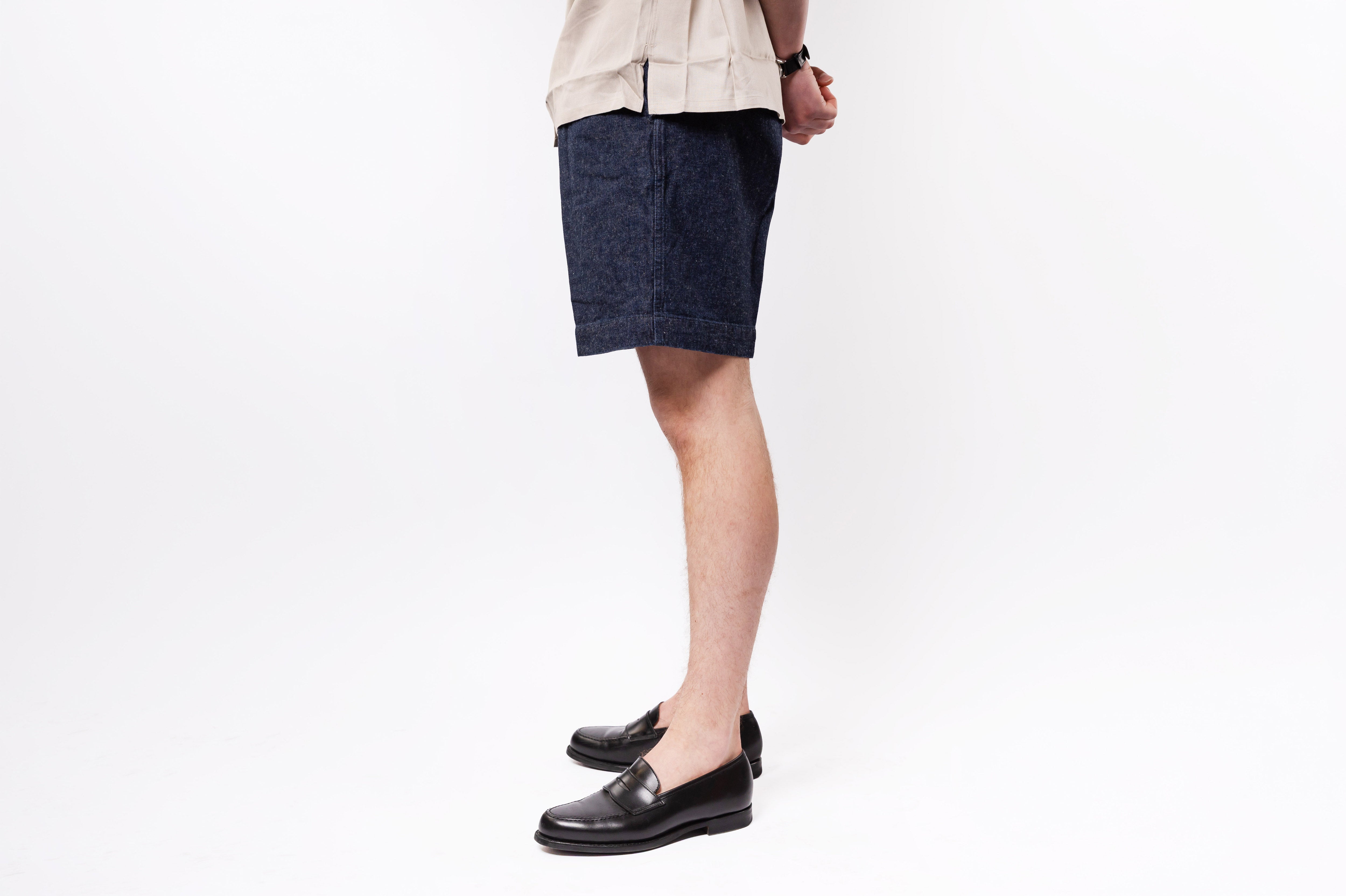 Person wearing dark denim shorts and black shoes on a white background