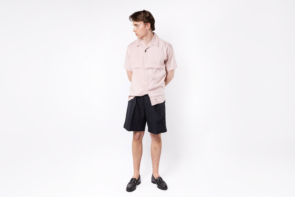 Person wearing a light pink shirt and black shorts on a white background