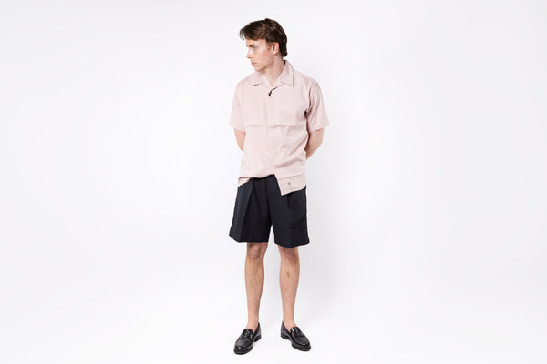 Person wearing a light pink shirt and black shorts on a white background