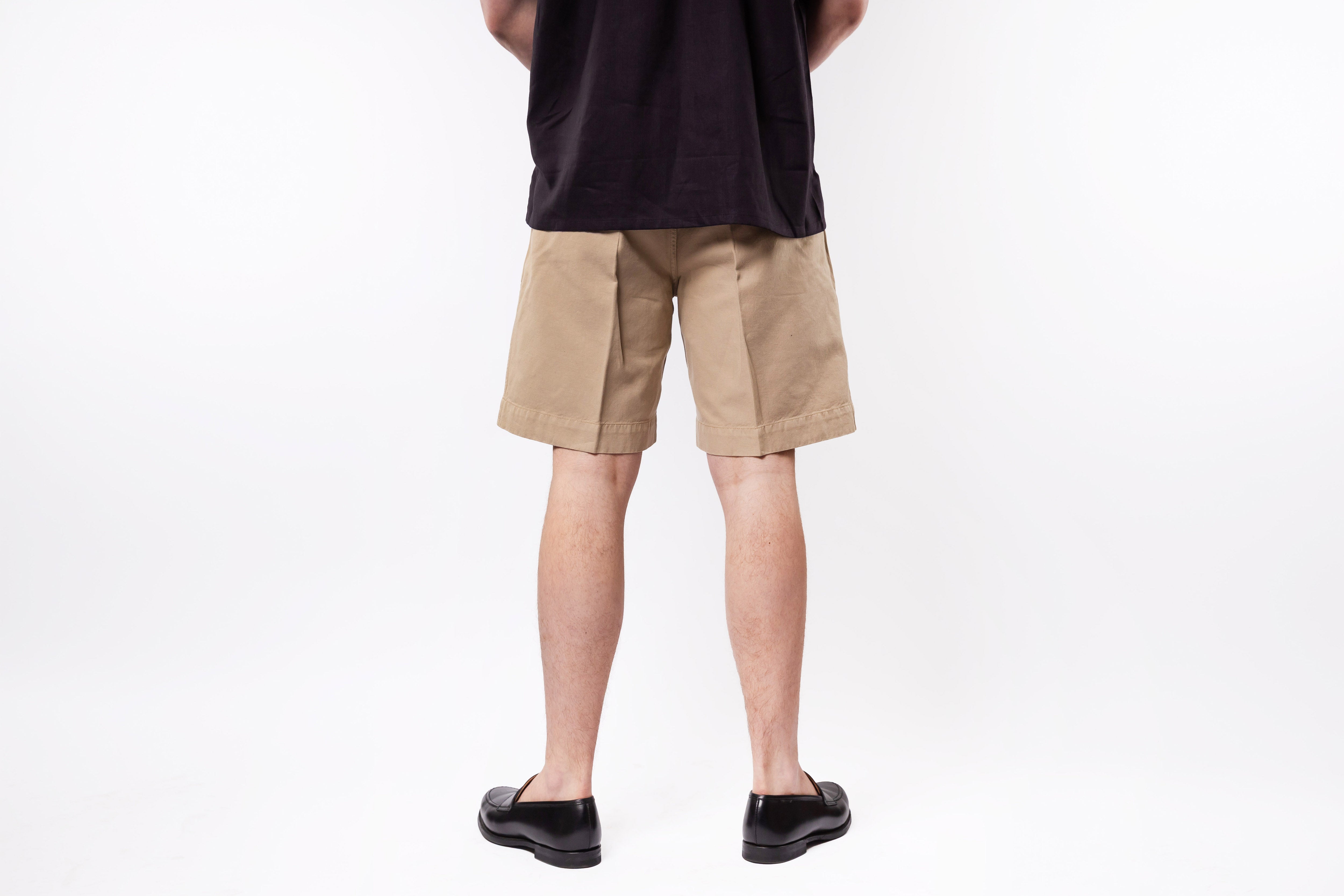Person wearing beige shorts and black shoes on a white background
