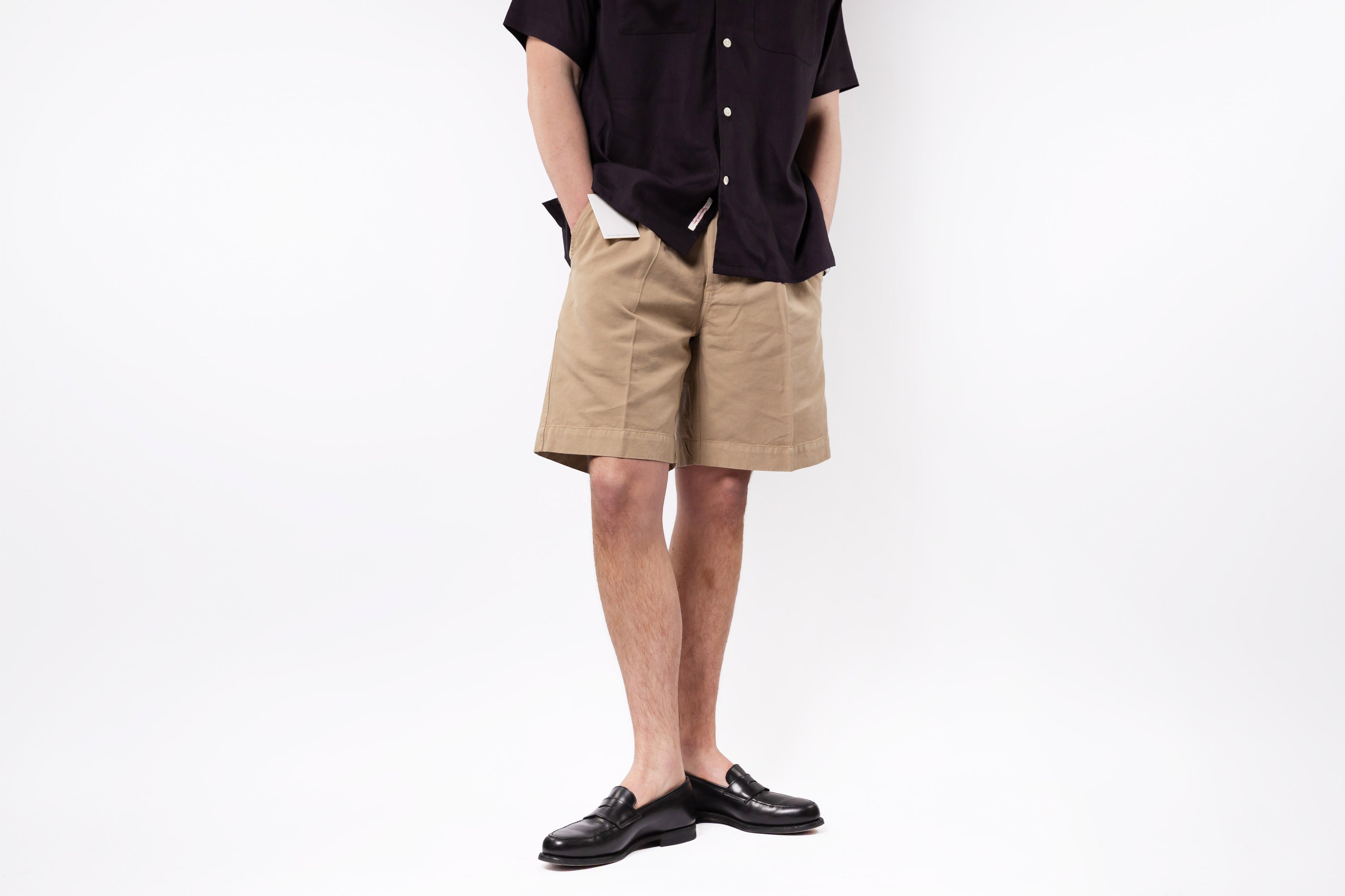 Person wearing beige shorts and black shoes on a white background