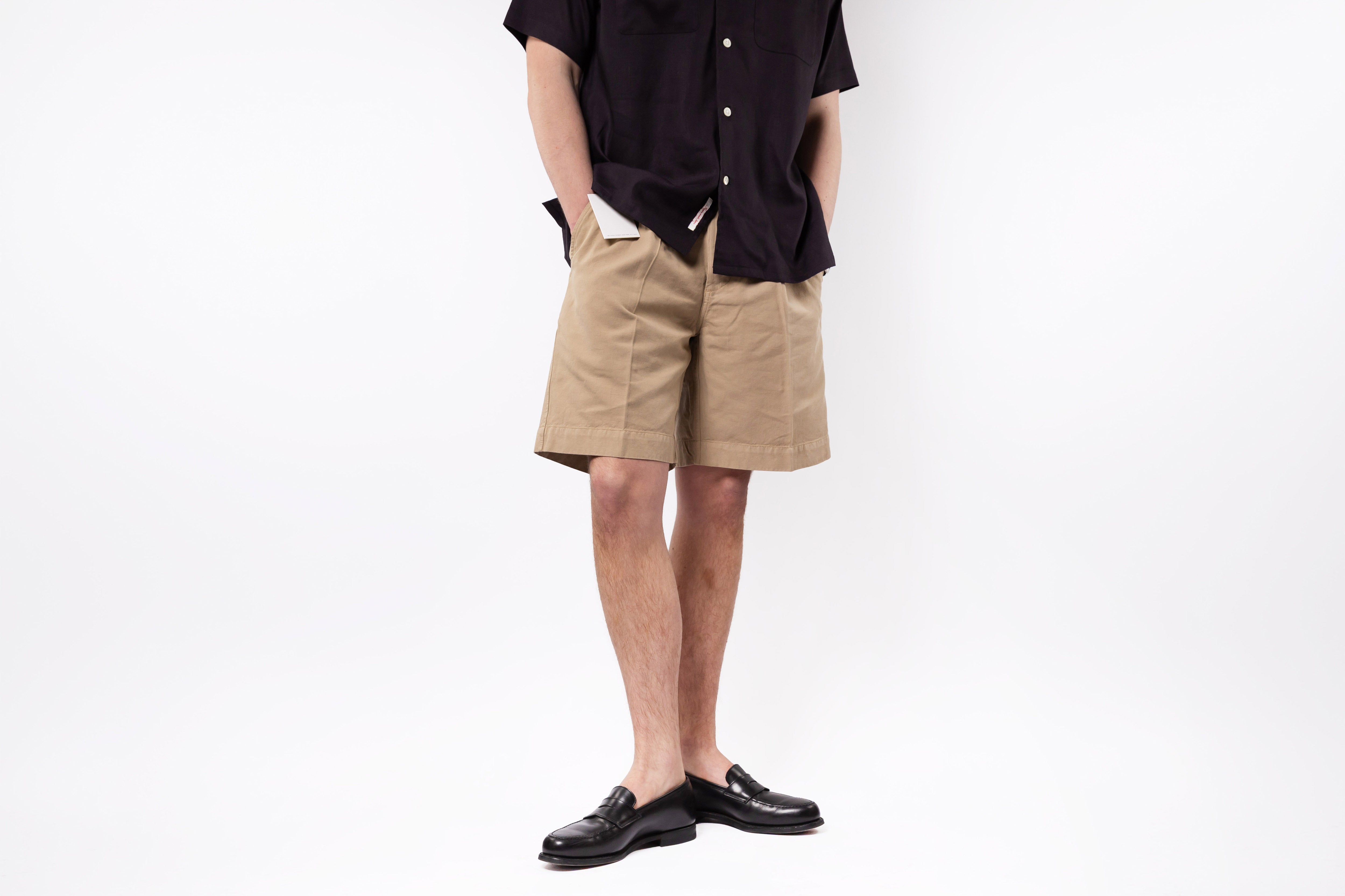 Person wearing beige shorts and black shoes on a white background