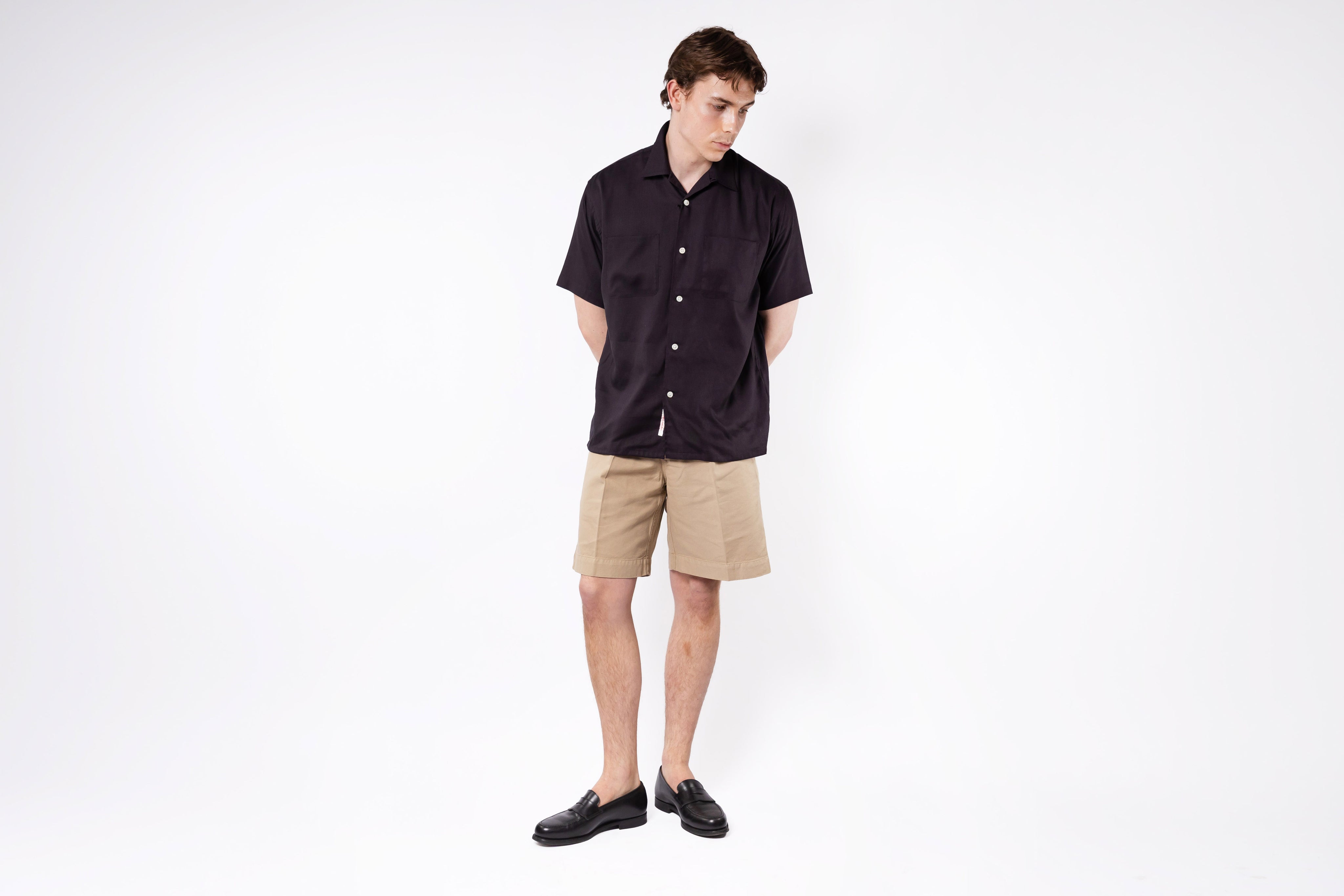 Person wearing a black shirt and beige shorts on a white background