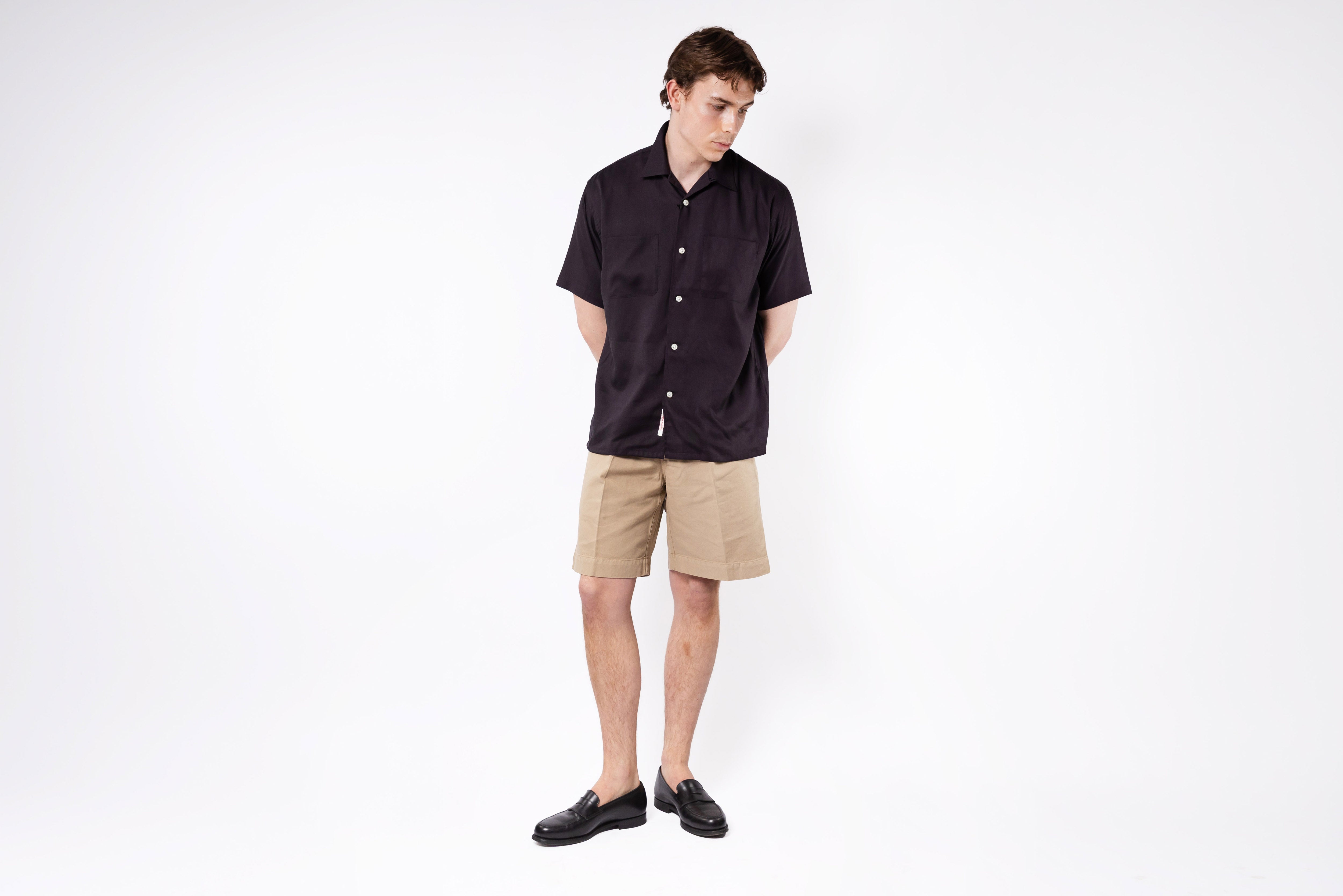 Person wearing a black shirt and beige shorts on a white background