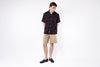 Person wearing a black shirt and beige shorts on a white background