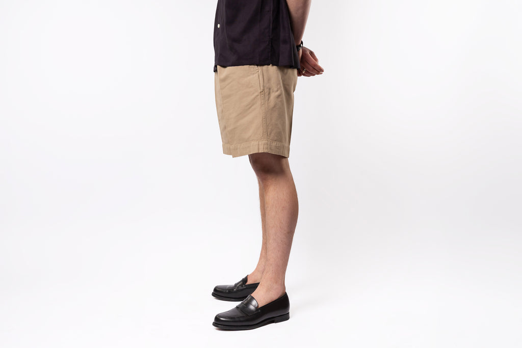 Person wearing beige shorts and black shoes on a white background