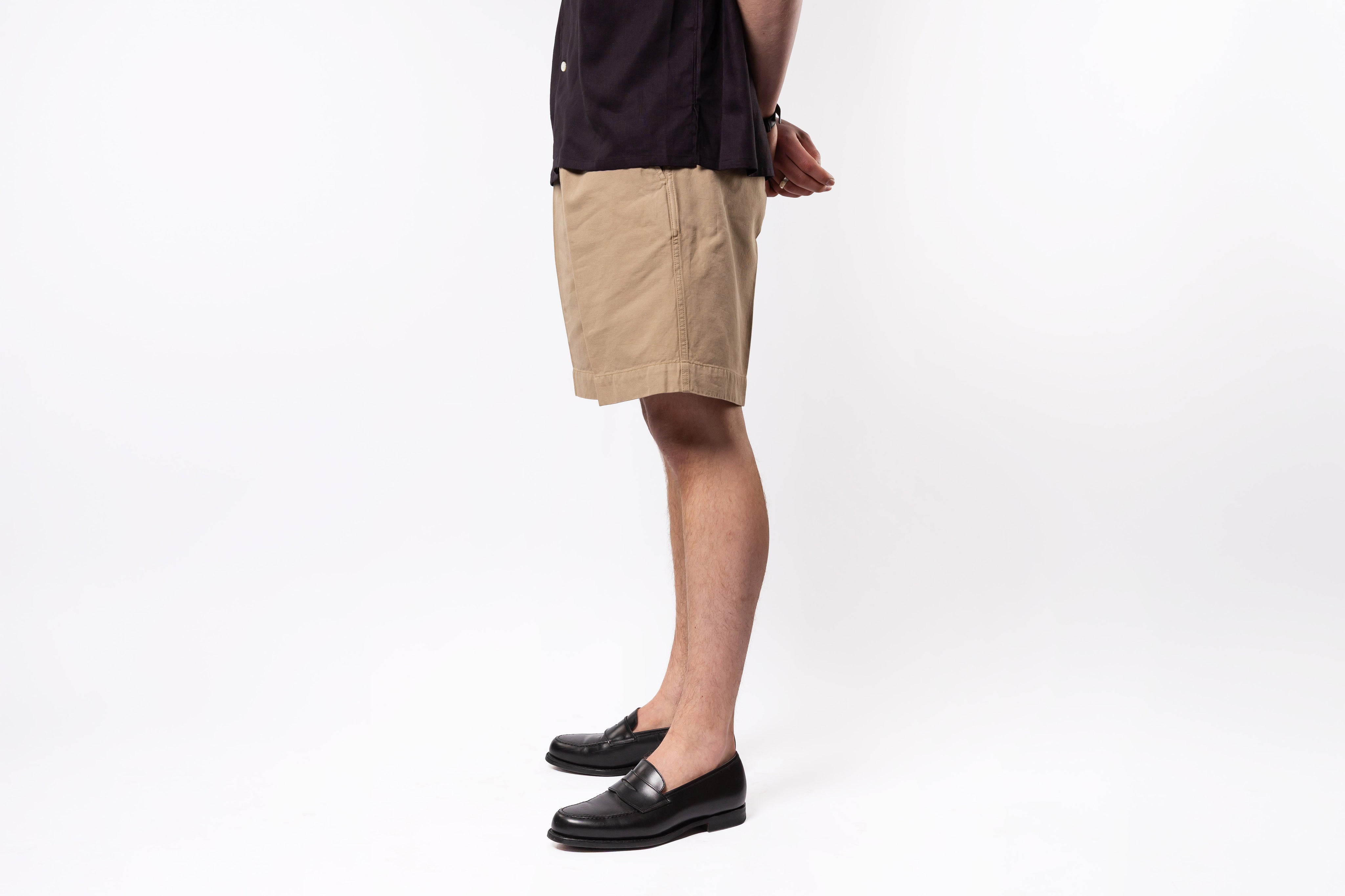 Person wearing beige shorts and black shoes on a white background