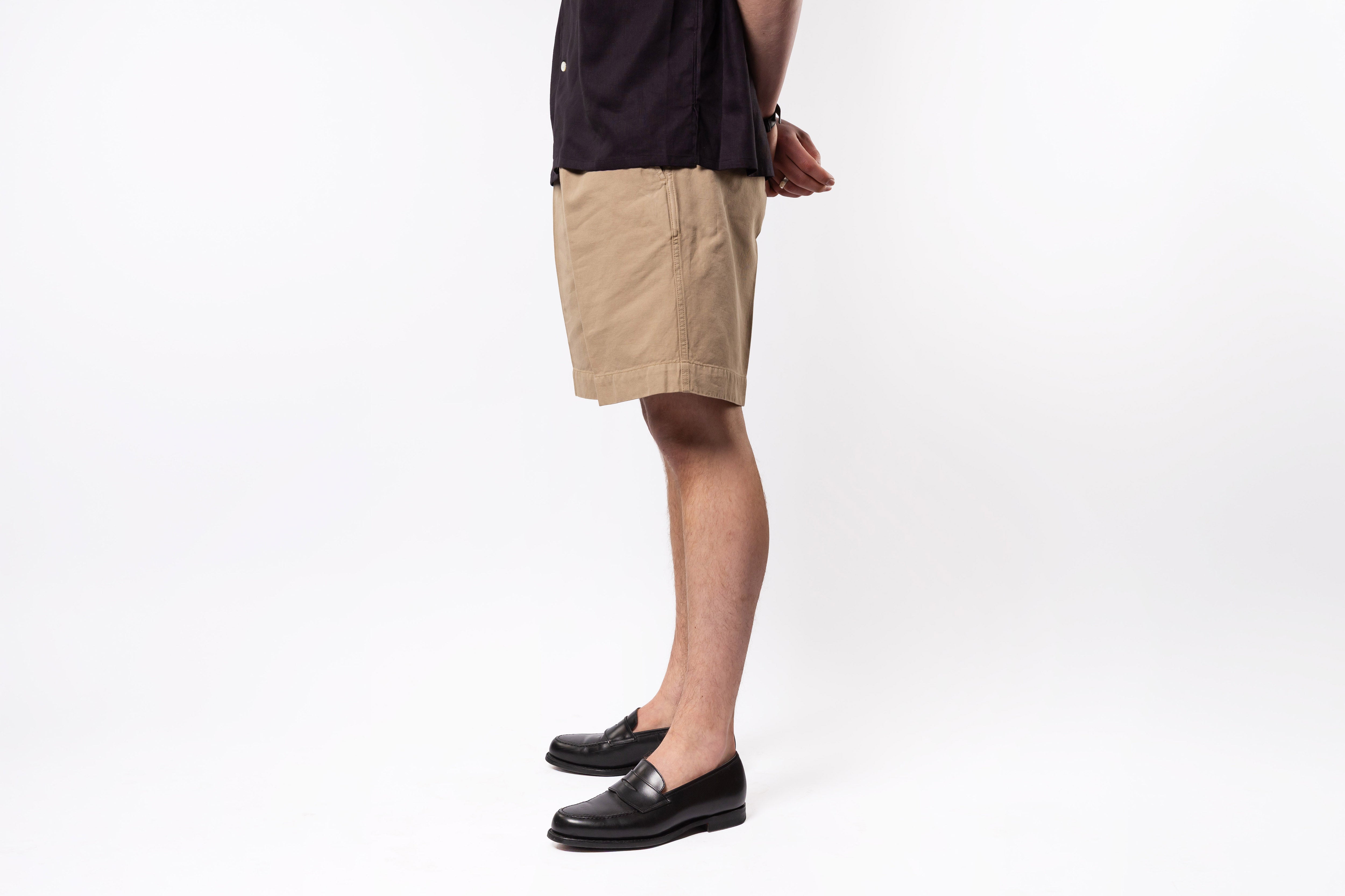 Person wearing beige shorts and black shoes on a white background