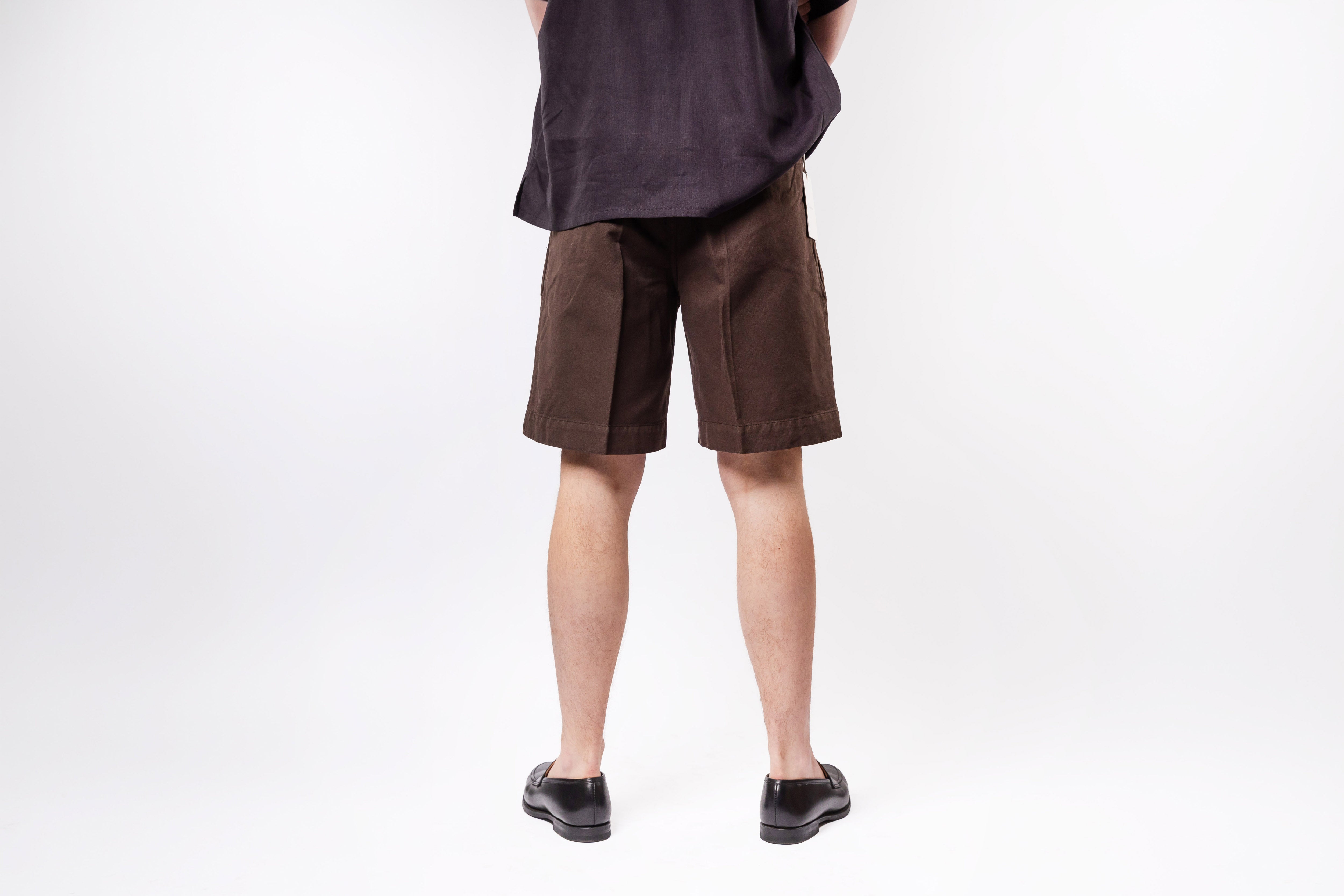 Person wearing brown shorts and black shoes on a white background