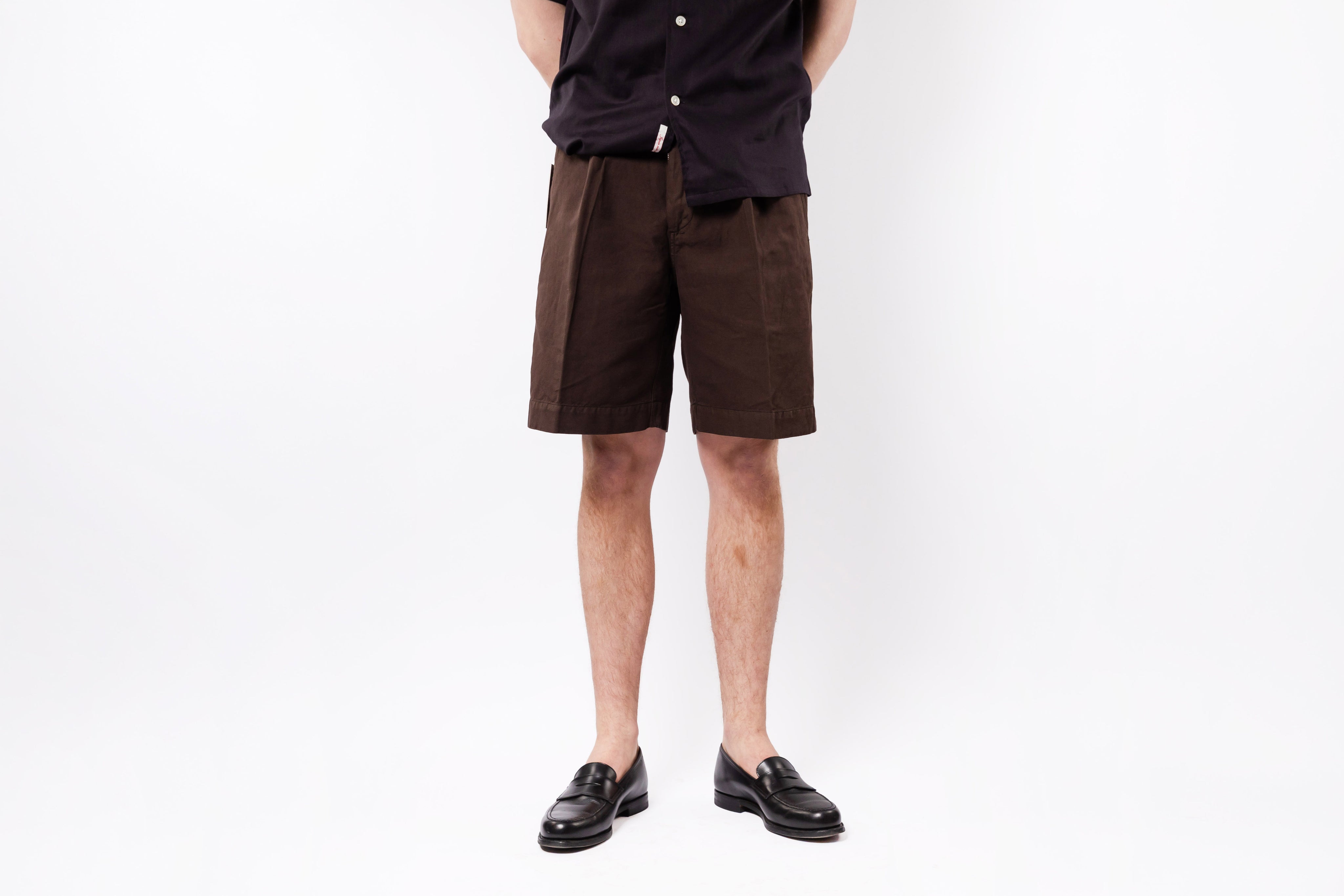 Person wearing brown shorts and black shoes on a white background