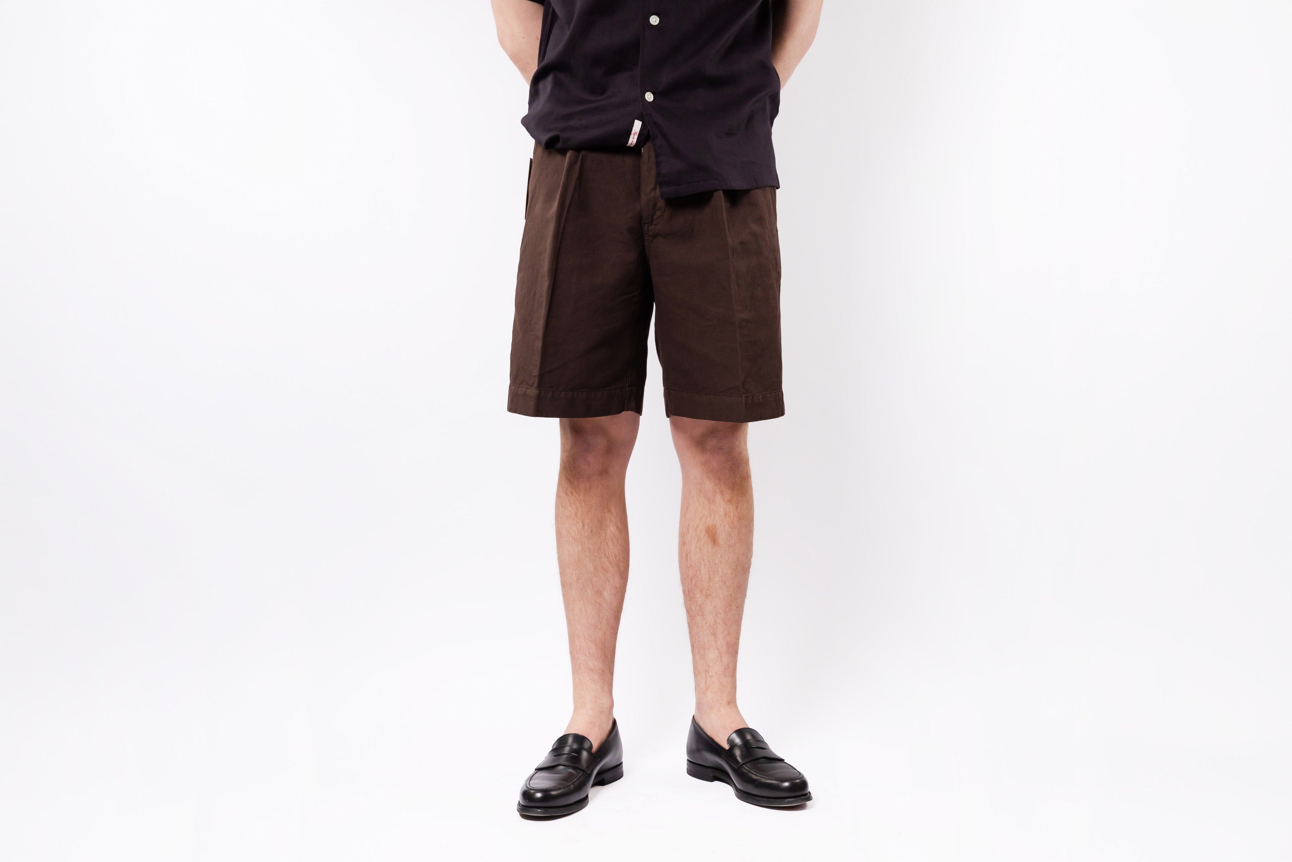 Person wearing brown shorts and black shoes on a white background